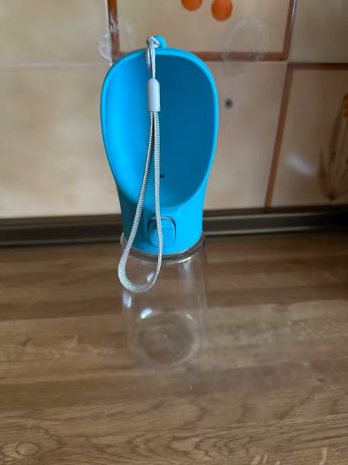 The blue dog water bottle standing on a wooden floor with its wrist strap hanging down
