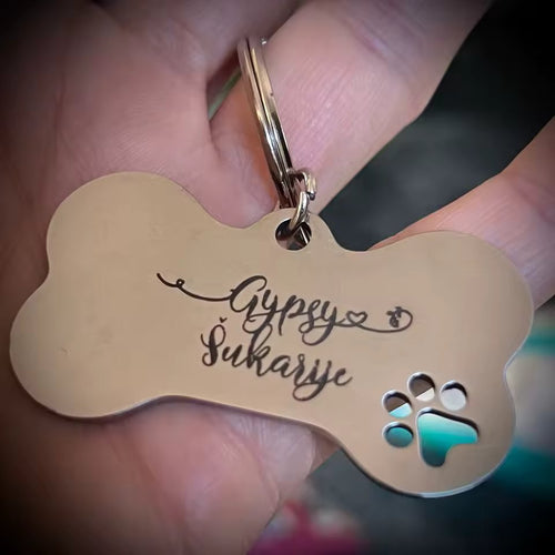 An engraved bone-shaped dog tag held in a hand, with the paw print cut clean through the corner